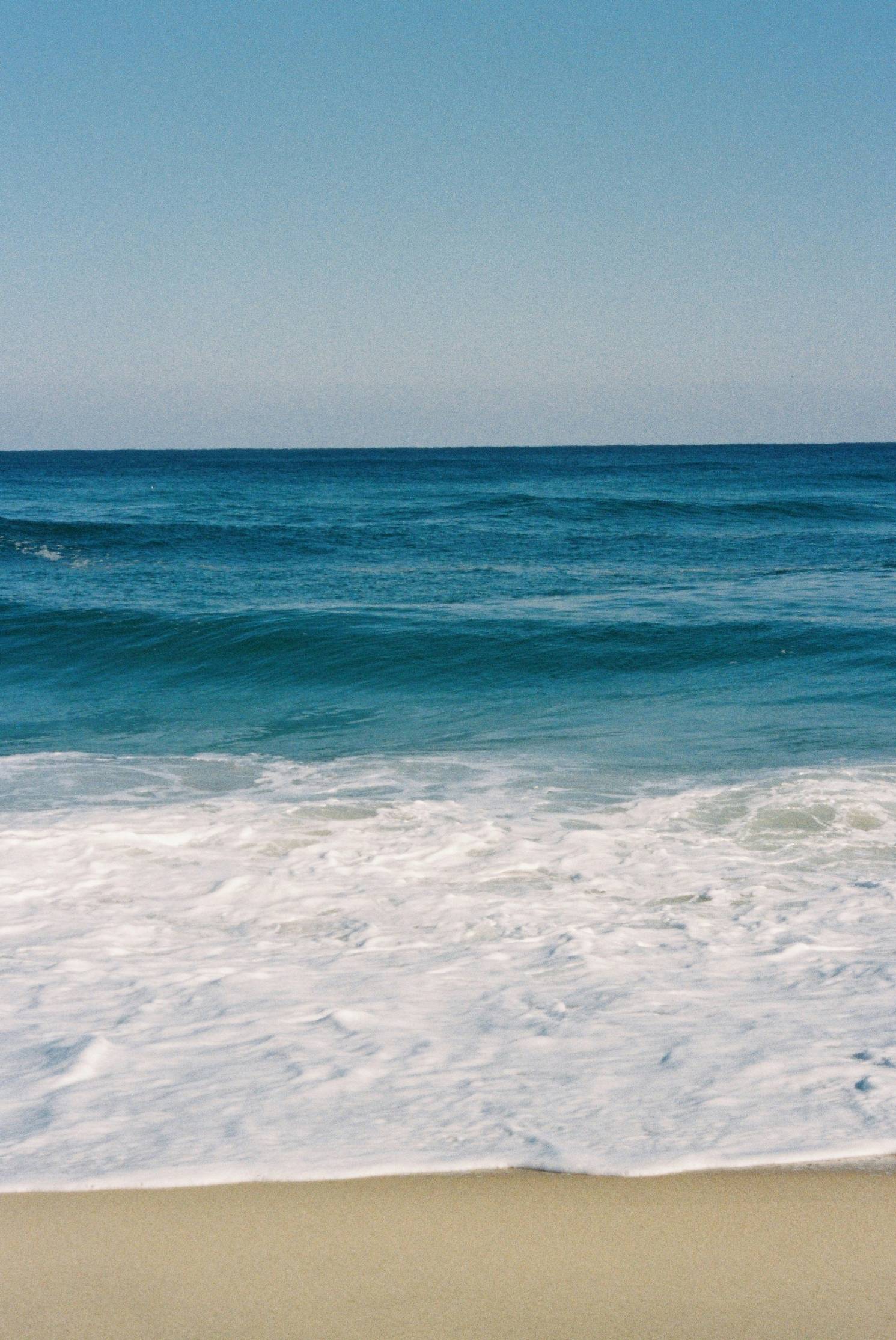 Waves crash on the sandy beach under a bright sky.
